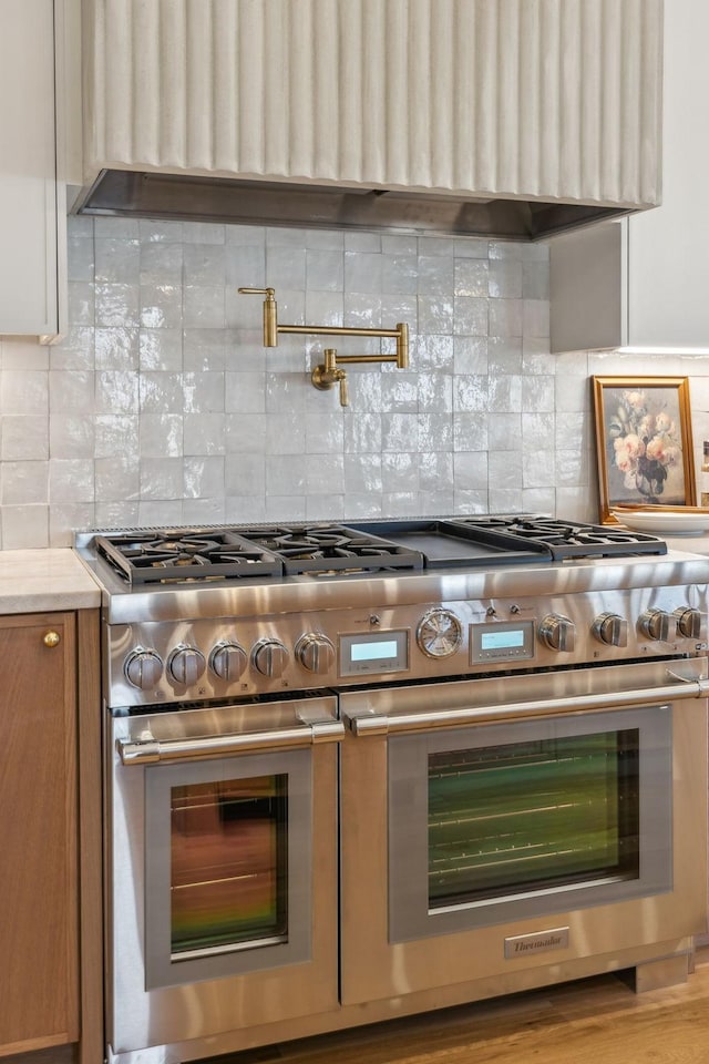 kitchen with decorative backsplash, brown cabinets, premium range hood, and range with two ovens