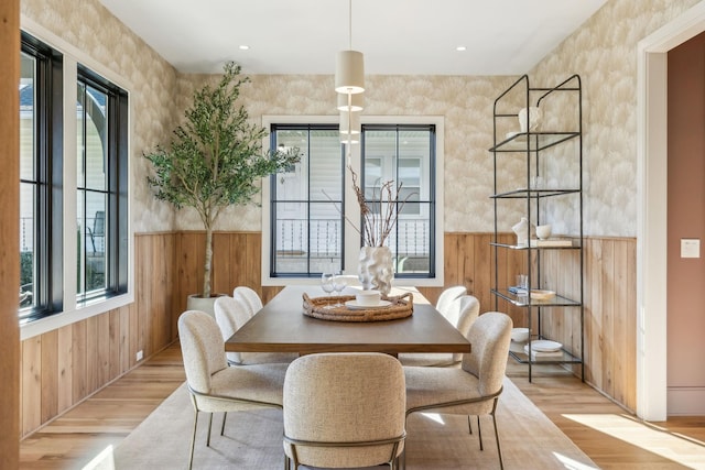 dining space with a healthy amount of sunlight, wood walls, and light wood-style floors