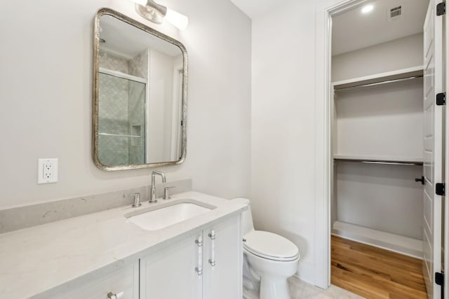 bathroom featuring vanity, visible vents, a spacious closet, toilet, and a shower with door