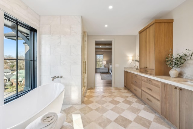 ensuite bathroom featuring tile walls, a freestanding bath, double vanity, tile patterned floors, and ensuite bath