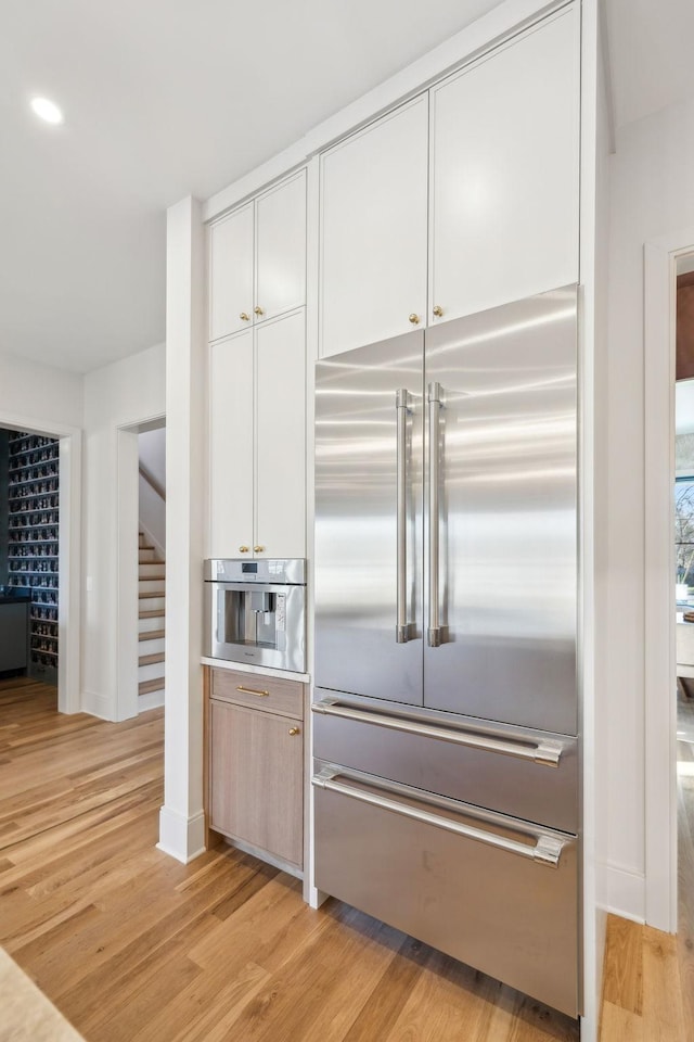 kitchen featuring baseboards, light wood-style flooring, stainless steel appliances, light countertops, and white cabinetry