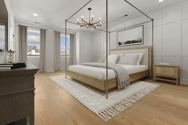 bedroom with a decorative wall, a notable chandelier, recessed lighting, and light wood finished floors