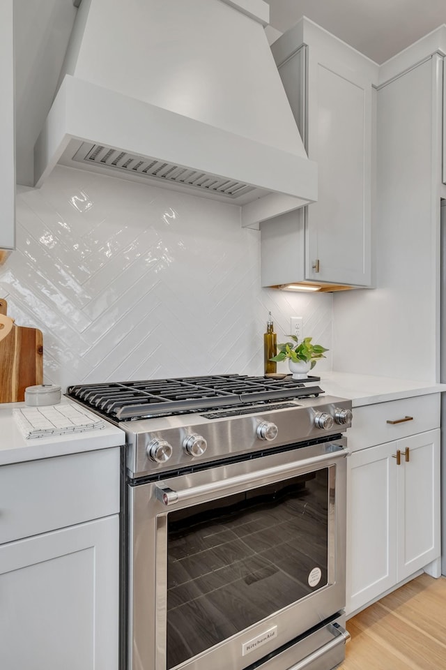 kitchen with custom exhaust hood, decorative backsplash, light countertops, light wood-style floors, and stainless steel gas stove