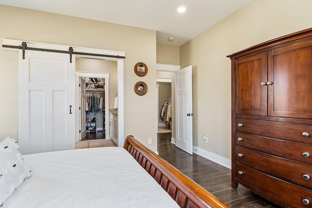 bedroom featuring a walk in closet, baseboards, a closet, a barn door, and dark wood-style floors