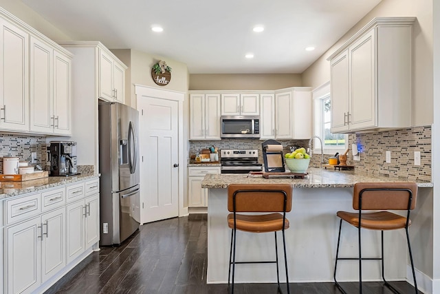 kitchen with dark wood-type flooring, a kitchen bar, light stone counters, a peninsula, and stainless steel appliances