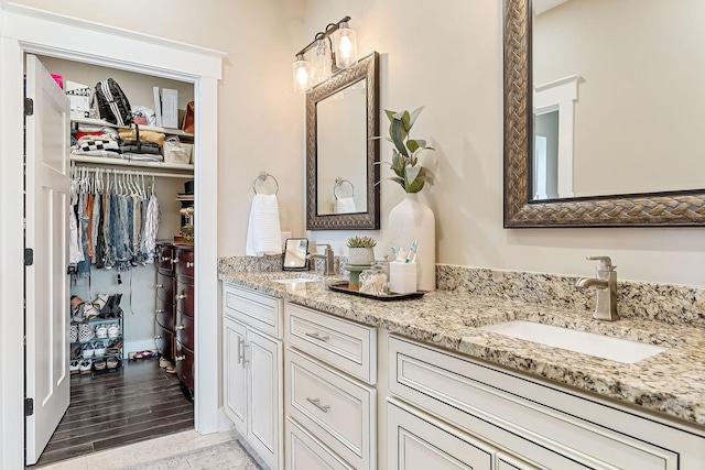 full bathroom featuring double vanity, a spacious closet, wood finished floors, and a sink