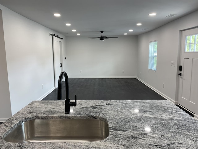 kitchen with a barn door, recessed lighting, stone countertops, a ceiling fan, and a sink