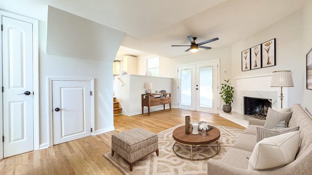 living room featuring a high end fireplace, stairway, light wood-style floors, baseboards, and ceiling fan