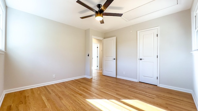 unfurnished bedroom with attic access, baseboards, light wood finished floors, and ceiling fan