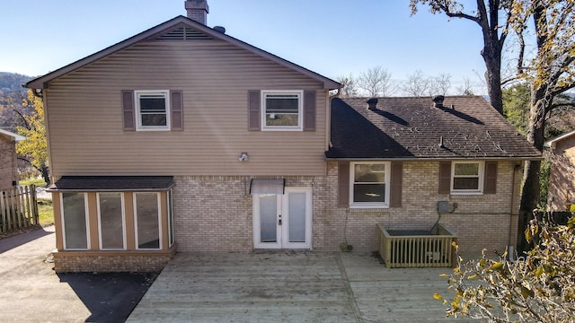 rear view of house with a deck, french doors, brick siding, and a chimney