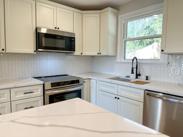 kitchen with light stone countertops, a sink, white cabinets, appliances with stainless steel finishes, and tasteful backsplash