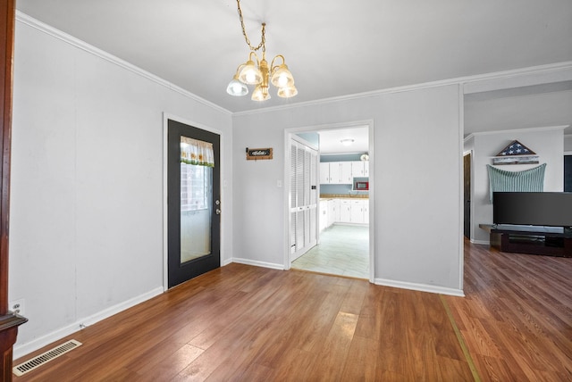 interior space featuring wood finished floors, baseboards, visible vents, ornamental molding, and a notable chandelier