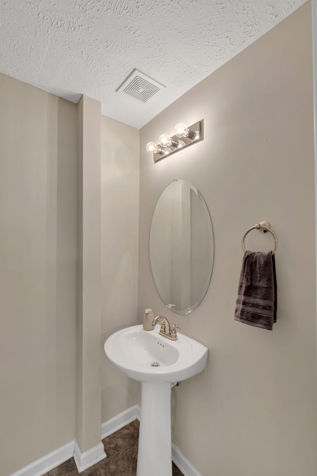 bathroom featuring a sink, baseboards, visible vents, and a textured ceiling