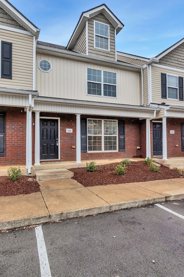 townhome / multi-family property featuring uncovered parking, brick siding, and covered porch