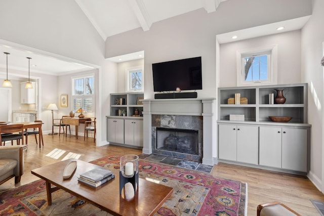 living area with a tiled fireplace, vaulted ceiling with beams, baseboards, and light wood finished floors