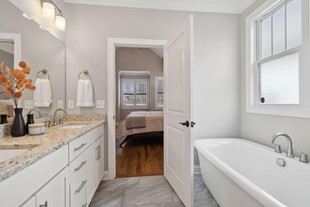 bathroom with double vanity, a freestanding tub, connected bathroom, and a sink