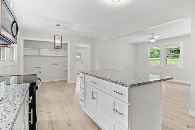 kitchen featuring stainless steel microwave, light wood-style flooring, light stone counters, and a center island