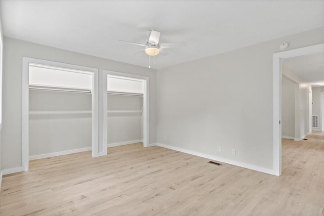 unfurnished bedroom with baseboards, visible vents, multiple closets, and light wood-type flooring