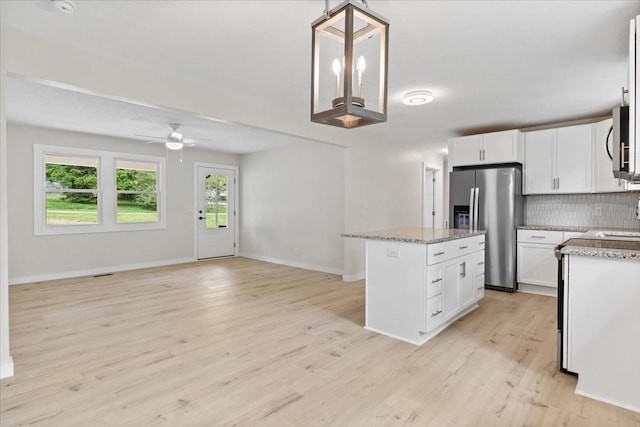 kitchen with a ceiling fan, a kitchen island, stainless steel appliances, tasteful backsplash, and light wood-type flooring