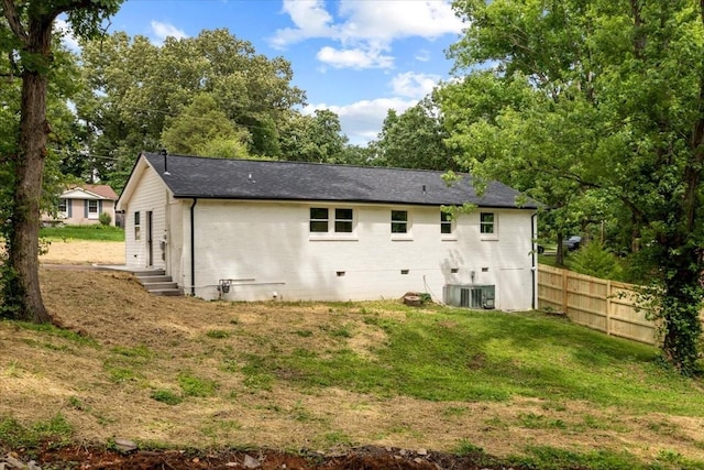 rear view of property with brick siding, a shingled roof, fence, central air condition unit, and a lawn