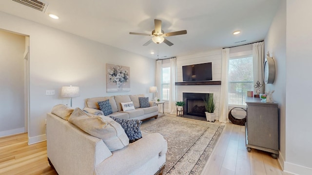 living room with visible vents, a large fireplace, baseboards, ceiling fan, and wood finished floors