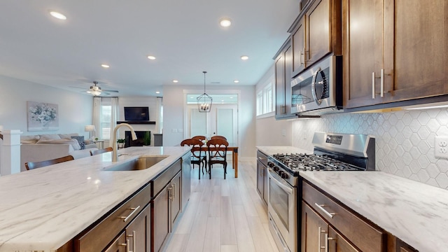 kitchen with a sink, a fireplace, light stone countertops, and stainless steel appliances