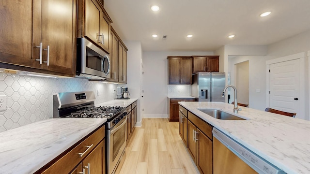 kitchen with light wood-type flooring, light stone counters, recessed lighting, stainless steel appliances, and a sink