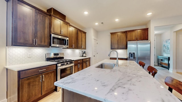 kitchen with a sink, light stone countertops, tasteful backsplash, and stainless steel appliances