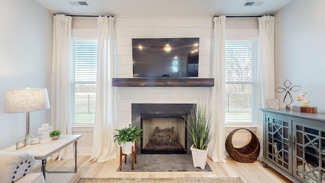 living room featuring visible vents, a large fireplace, a healthy amount of sunlight, and wood finished floors