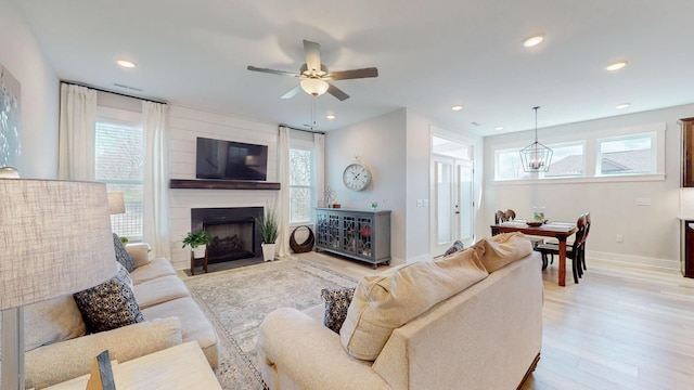 living room featuring ceiling fan with notable chandelier, a healthy amount of sunlight, and light wood finished floors