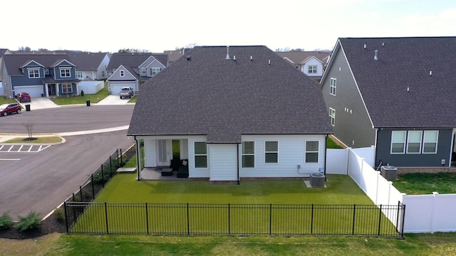 back of house with a residential view, a lawn, central AC, and a fenced backyard