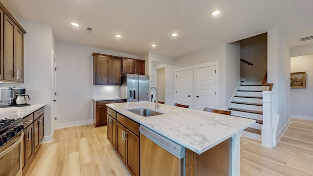 kitchen featuring a sink, light stone counters, light wood finished floors, and stainless steel appliances