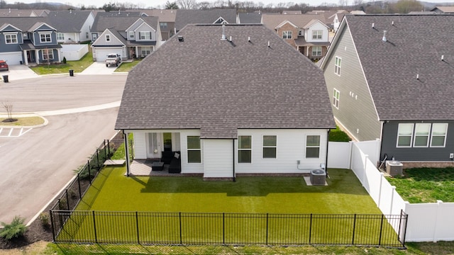 back of property with a lawn, a residential view, a fenced backyard, and a shingled roof