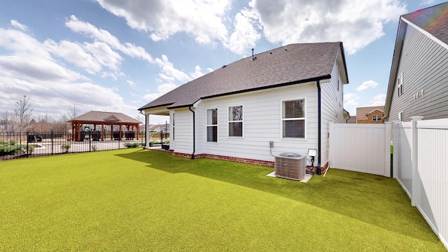 back of property with fence, roof with shingles, a gazebo, central AC unit, and a yard