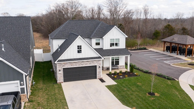 view of front of house featuring fence, roof with shingles, an attached garage, a front lawn, and board and batten siding