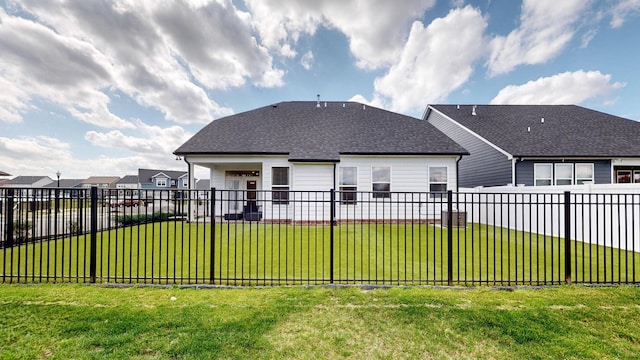 rear view of property featuring a lawn, roof with shingles, and fence