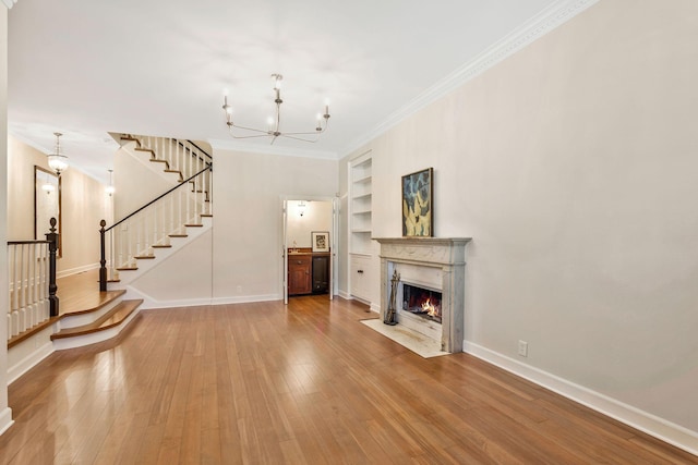 unfurnished living room featuring a chandelier, built in shelves, baseboards, and hardwood / wood-style flooring