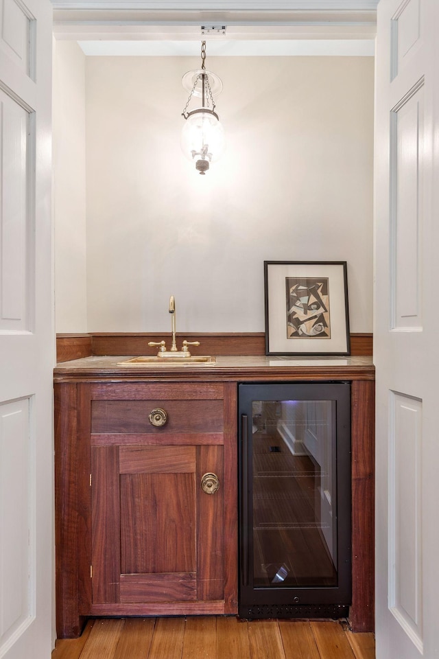 bar with hanging light fixtures, light wood-style flooring, beverage cooler, and a sink