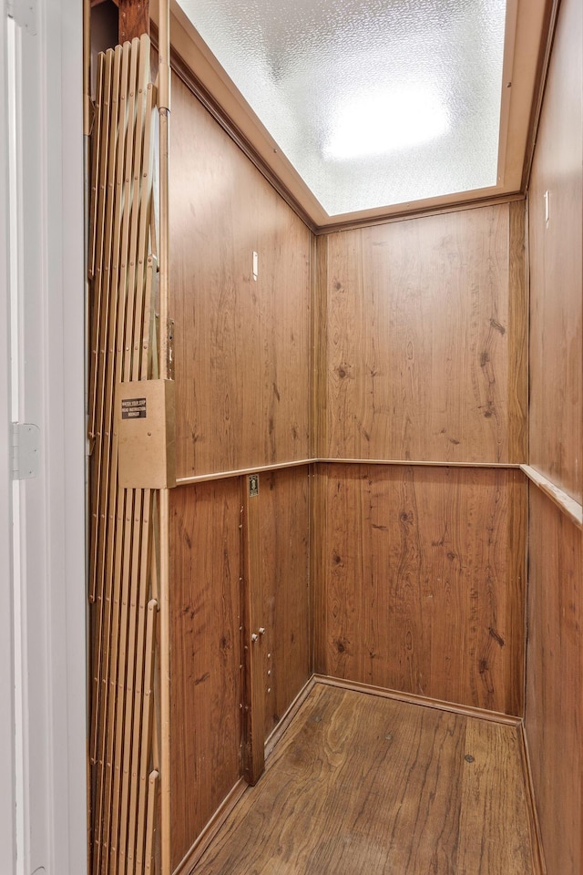 interior details with elevator, wooden walls, a textured ceiling, and wood finished floors