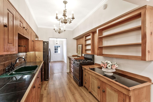 kitchen with black gas stove, a chandelier, ornamental molding, freestanding refrigerator, and a sink