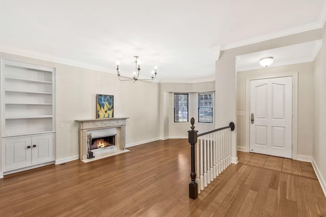 entryway with wood finished floors, baseboards, an inviting chandelier, a fireplace with flush hearth, and crown molding