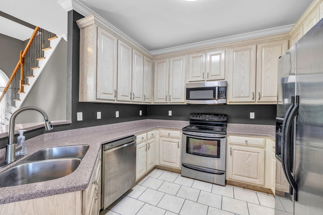 kitchen with ornamental molding, light tile patterned floors, appliances with stainless steel finishes, cream cabinetry, and a sink