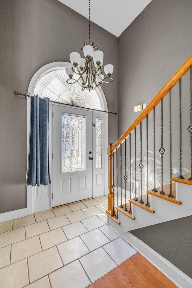 tiled foyer entrance featuring stairway, baseboards, high vaulted ceiling, and a chandelier