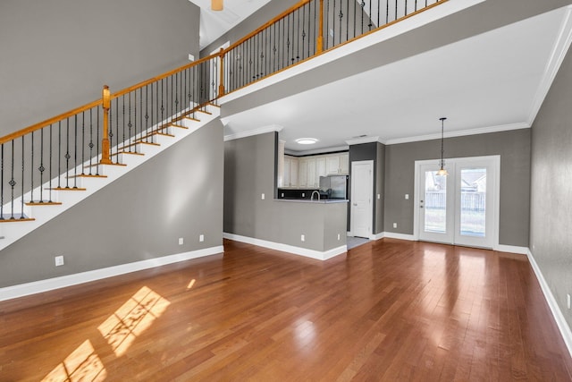 unfurnished living room with baseboards, a high ceiling, wood finished floors, and ornamental molding