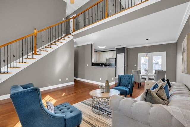 living room featuring wood finished floors, crown molding, baseboards, a towering ceiling, and stairs