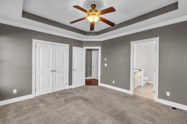 unfurnished bedroom featuring a raised ceiling, carpet flooring, baseboards, and a closet