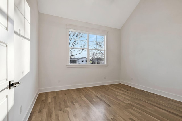 unfurnished room featuring vaulted ceiling, wood finished floors, and baseboards