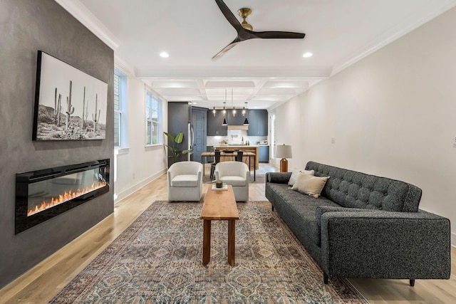 living room with light wood-type flooring, coffered ceiling, a glass covered fireplace, and a ceiling fan