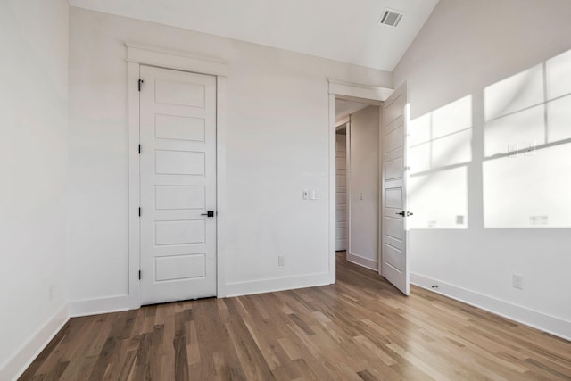 unfurnished bedroom with visible vents, wood finished floors, baseboards, and lofted ceiling