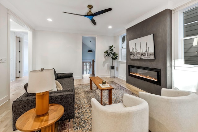 living area featuring a ceiling fan, wood finished floors, recessed lighting, a large fireplace, and crown molding